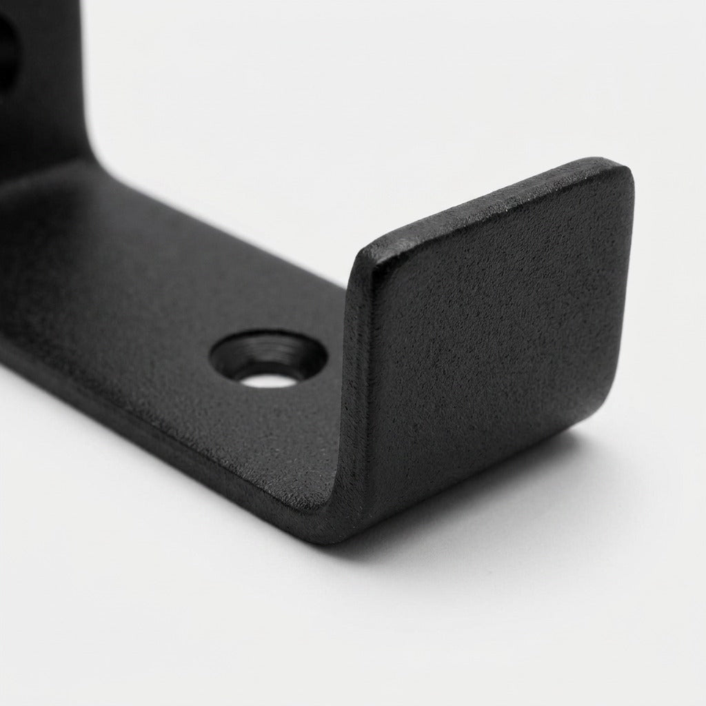 Close-up of Entrepot La Grange matte black steel J-shelf bracket showing curved lip and screw hole.